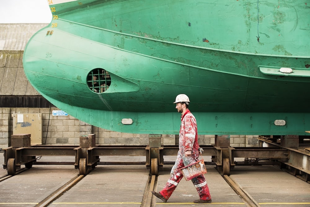 Male ship painter carrying paint cans in ship painters yard