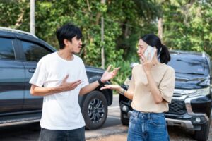 Two drivers arguing after a car accident. The woman is on the phone, asking “what happens if an uninsured driver hits you in Louisiana?”