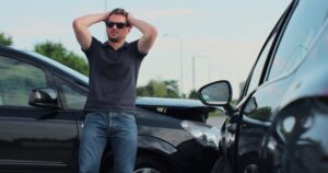Man with his hands on his head in frustration as he stands next to two crashed cars after being hit by an uninsured driver in New Orleans.