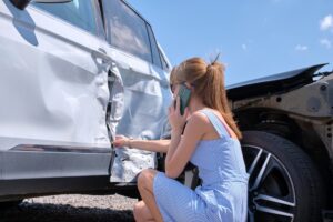 A woman on the phone, examining the damage of a car accident in New Orleans, wondering if she can sue.