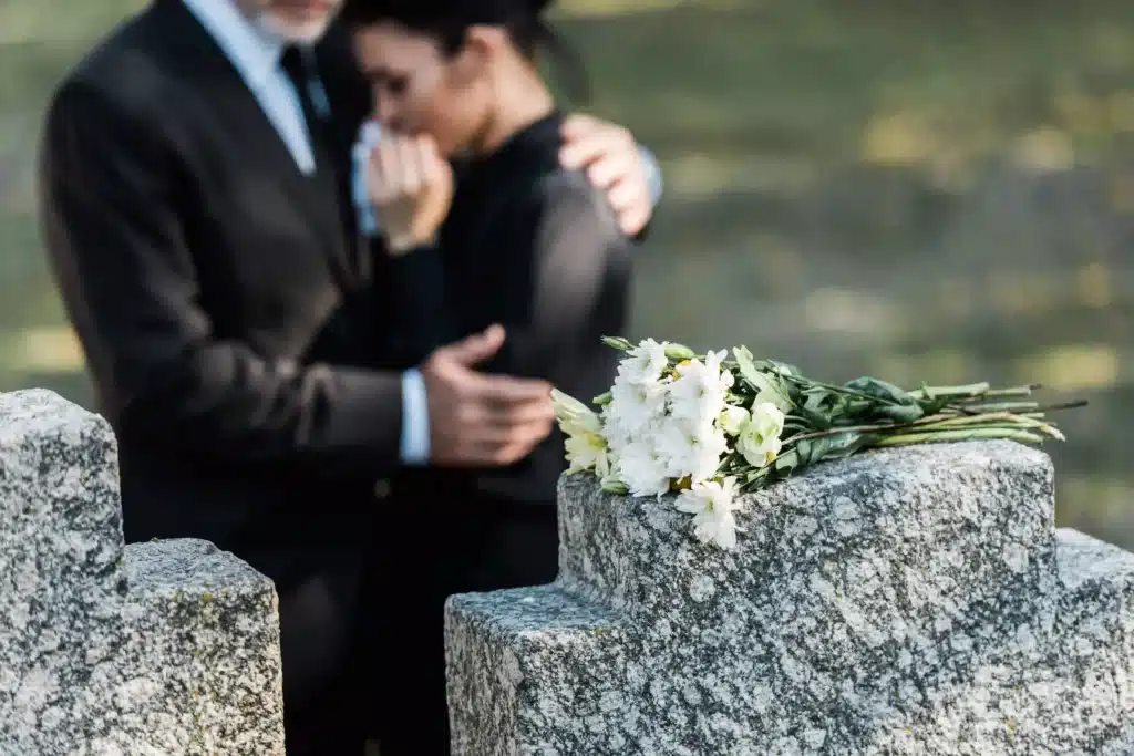 mourning-couple-at-grave-with-flowers-bouquet-