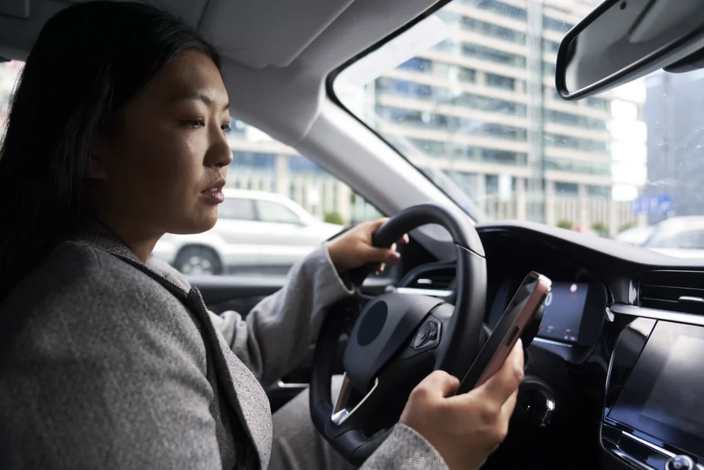 woman-driving-car-holding-cellphone-in-city-