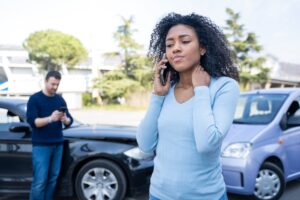 An injured woman on the phone, holding her neck after a car accident. How to obtain a police report after a car accident in Gretna, LA.