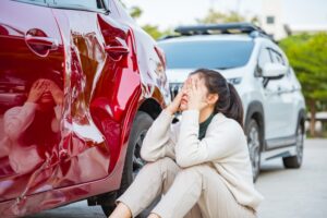A distressed woman sitting next to a damaged car after a car accident. How to obtain a police report after a car accident in Slidell, LA.