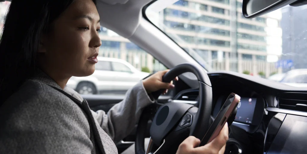 woman-driving-car-holding-cellphone-in-city-